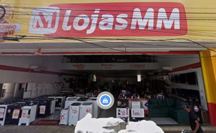 Fachada de loja com letreiro vermelho e branco exibindo o nome "Lojas MM" e diversos produtos em exposição na entrada
