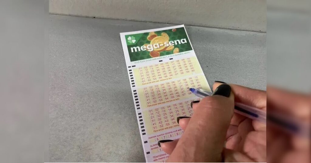 Mão com caneta marca números em volante da Mega-Sena sobre superfície cinza