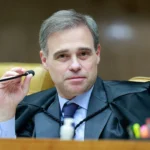 Um homem de toga segura um microfone em uma sala com cadeiras douradas