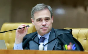 Um homem de toga segura um microfone em uma sala com cadeiras douradas