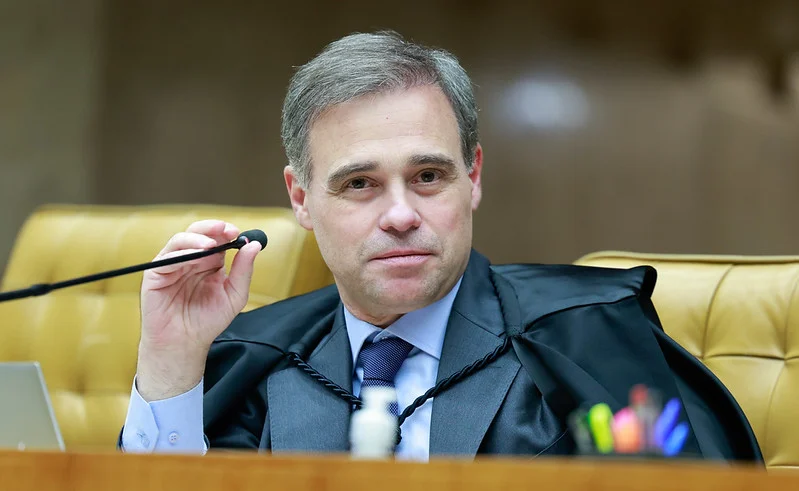 Um homem de toga segura um microfone em uma sala com cadeiras douradas