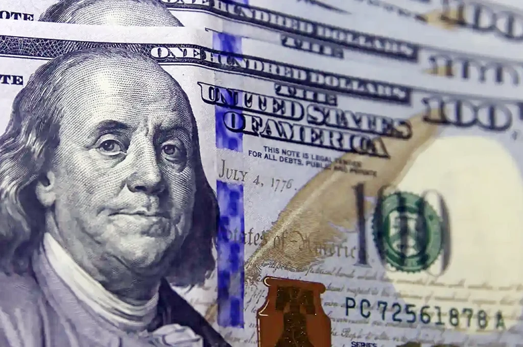 Cédulas de cem dólares dos Estados Unidos em destaque, com detalhes do retrato e inscrições visíveis