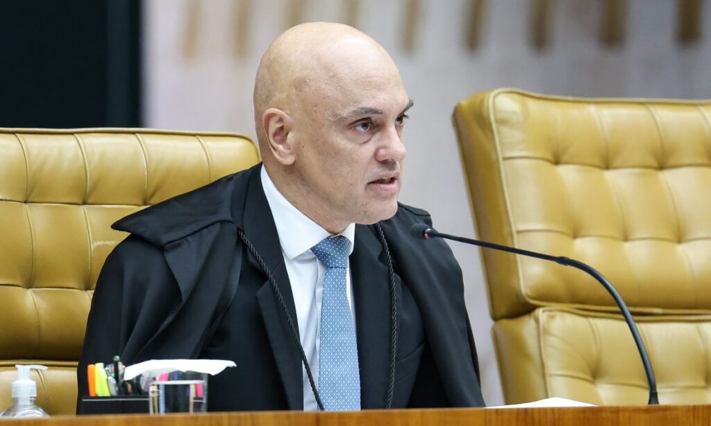 Um homem de toga sentado em cadeira de couro dourado fala em microfone em ambiente formal