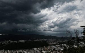 Nuvens escuras e densas cobrem o céu sobre uma cidade cercada por montanhas