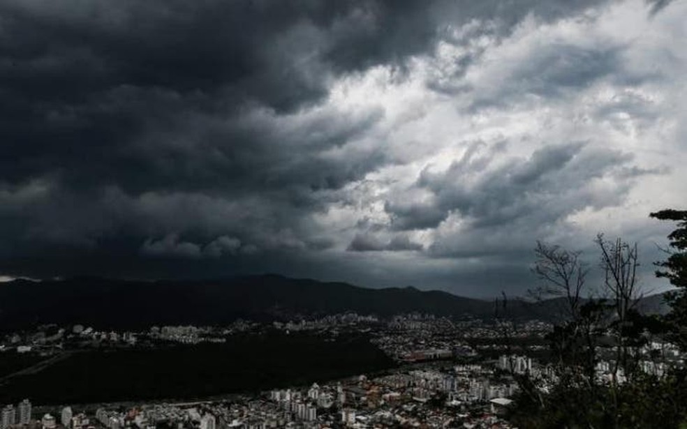 Nuvens escuras e densas cobrem o céu sobre uma cidade cercada por montanhas