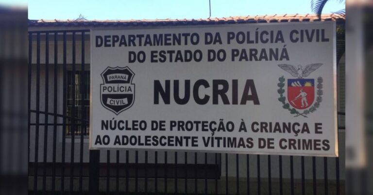 Placa do Núcleo de Proteção à Criança e ao Adolescente Vítimas de Crimes da Polícia Civil do Paraná em frente a um prédio com grade metálica
