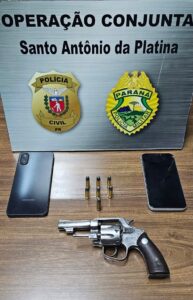 Revólver, munições e dois celulares sobre mesa em frente a placa de operação conjunta com emblemas de Polícia Civil e Polícia Militar do Paraná