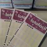 Três volantes da Lotofácil sobre uma superfície, com caixas de apostas ao fundo