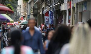 Pessoas caminham por rua movimentada com barracas e lojas ao fundo