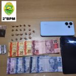 Objetos apreendidos dispostos sobre mesa, incluindo drogas, dinheiro, celulares e um estojo de cigarros