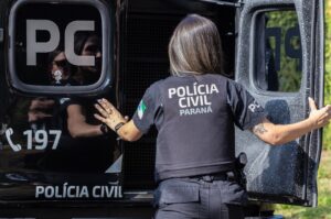 Mulher com uniforme da Polícia Civil do Paraná abre porta de veículo com inscrições "PC" e "197