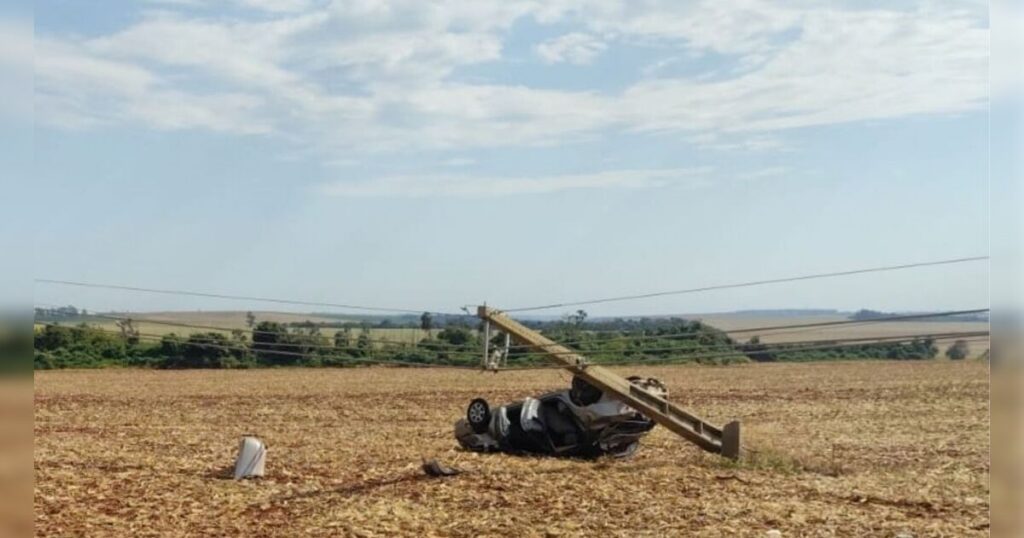 Veículo capotado em campo seco com poste de energia danificado e inclinado ao lado