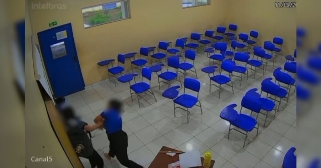 Duas pessoas se agarram em uma sala de aula com cadeiras azuis e portas azuis