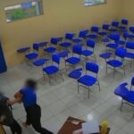 Duas pessoas se agarram em uma sala de aula com cadeiras azuis e portas azuis