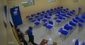 Duas pessoas se agarram em uma sala de aula com cadeiras azuis e portas azuis