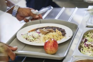Mão segura bandeja com prato de comida e maçã em restaurante coletivo
