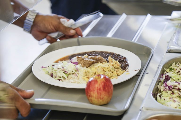 Mão segura bandeja com prato de comida e maçã em restaurante coletivo