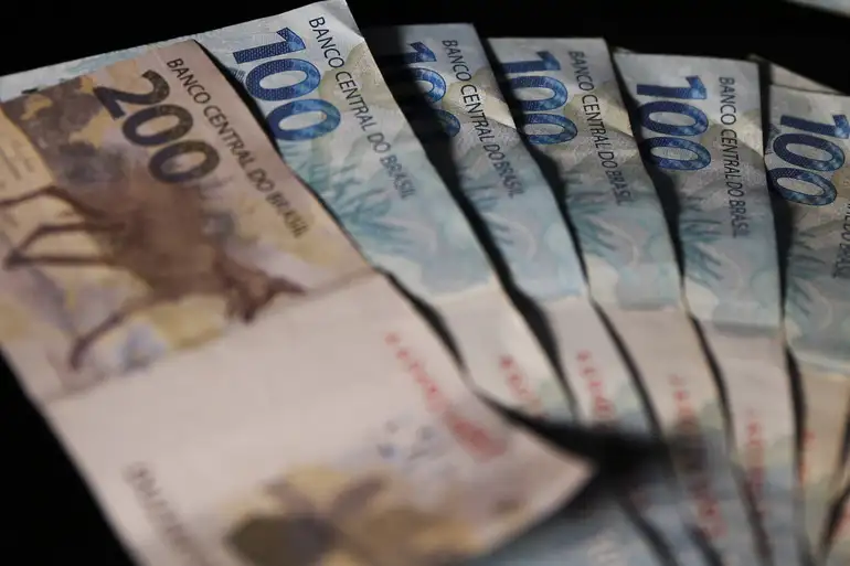 Notas de cem e duzentos reais do Banco Central do Brasil dispostas sobre fundo escuro