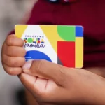 Mãos seguram cartão do Programa Bolsa Família com design colorido e logotipo visível