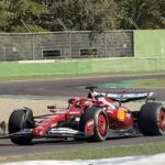 Um carro de Fórmula 1 vermelho com patrocínios visíveis em movimento em uma pista de corrida
