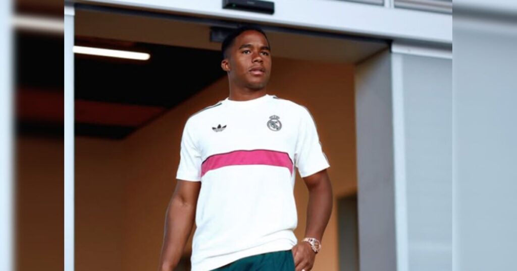 Um jovem com camisa branca do Real Madrid e detalhe rosa posa em ambiente interno