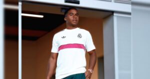 Um jovem com camisa branca do Real Madrid e detalhe rosa posa em ambiente interno