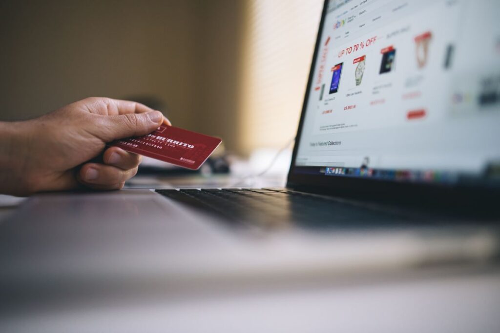 Mão segura cartão de crédito sobre laptop com página de compras online em tela