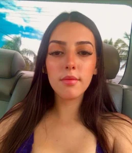 Uma mulher com cabelos longos sentada no banco de trás de um carro com palmeiras ao fundo