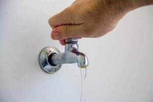 Uma mão abre uma torneira com pouca água saindo em um ambiente interno