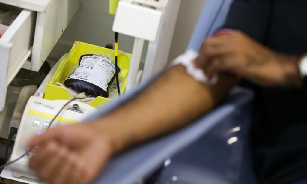 Mão de pessoa sendo limpa após doação de sangue com bolsa e equipamento ao lado