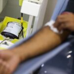 Mão de pessoa sendo limpa após doação de sangue com bolsa e equipamento ao lado
