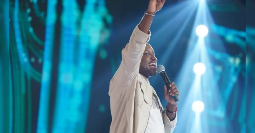 Um homem canta no palco com microfone na mão e braço erguido sob luzes de show