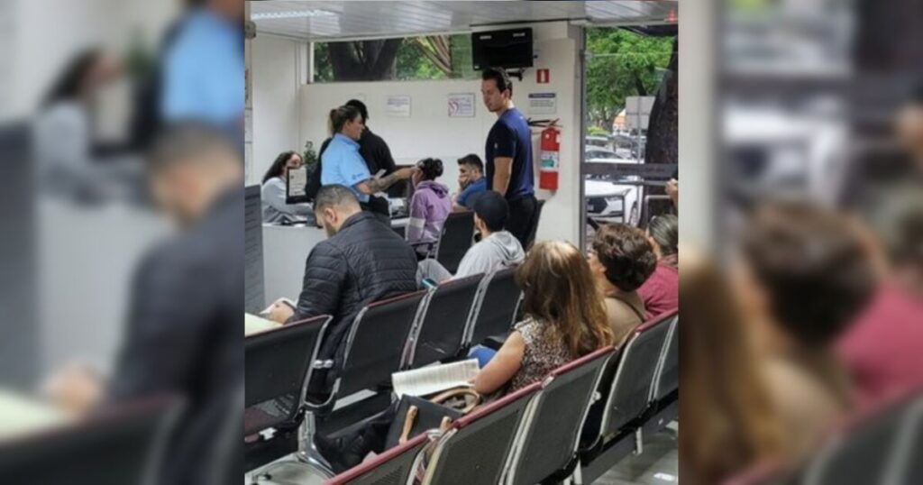 Um grupo de pessoas aguarda em cadeiras em um ambiente interno com atendimento em balcão