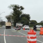 Caminhão e moto tombada em via com barreiras e cones, cercada por fita de isolamento