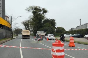 Caminhão e moto tombada em via com barreiras e cones, cercada por fita de isolamento