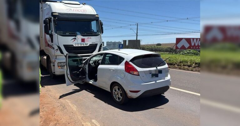 Caminhão e carro de passeio envolvidos em colisão na rodovia, com porta aberta e veículos parados no acostamento