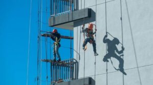 Dois trabalhadores em altura realizam serviço em fachada de edifício com equipamentos de segurança