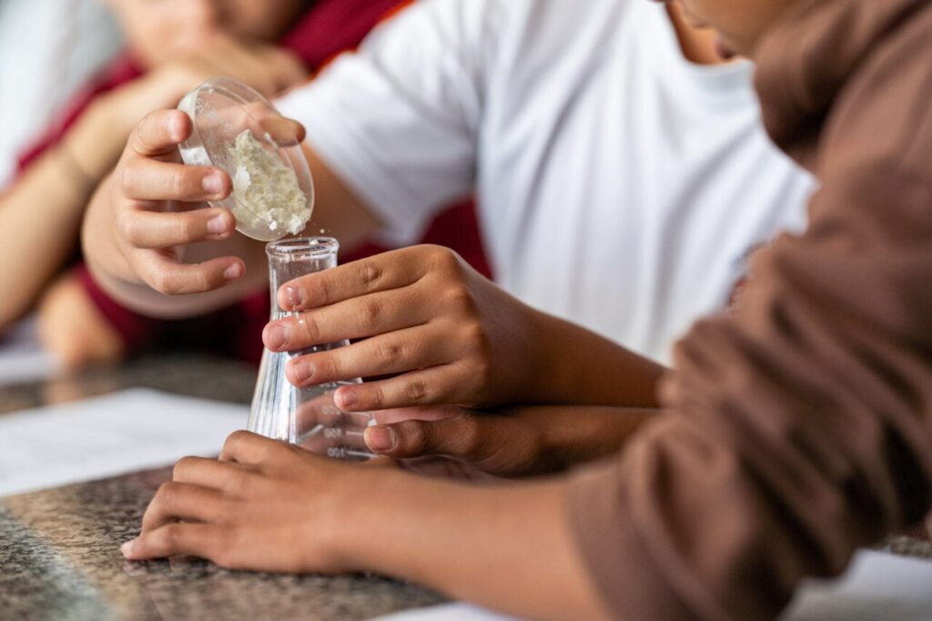 Mãos de crianças misturam substância em frasco de laboratório em atividade prática
