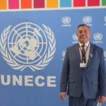 Um homem de terno posa em frente a um painel com o logo da UNECE em evento internacional