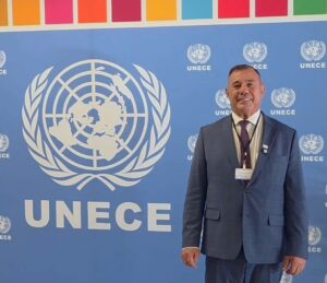 Um homem de terno posa em frente a um painel com o logo da UNECE em evento internacional