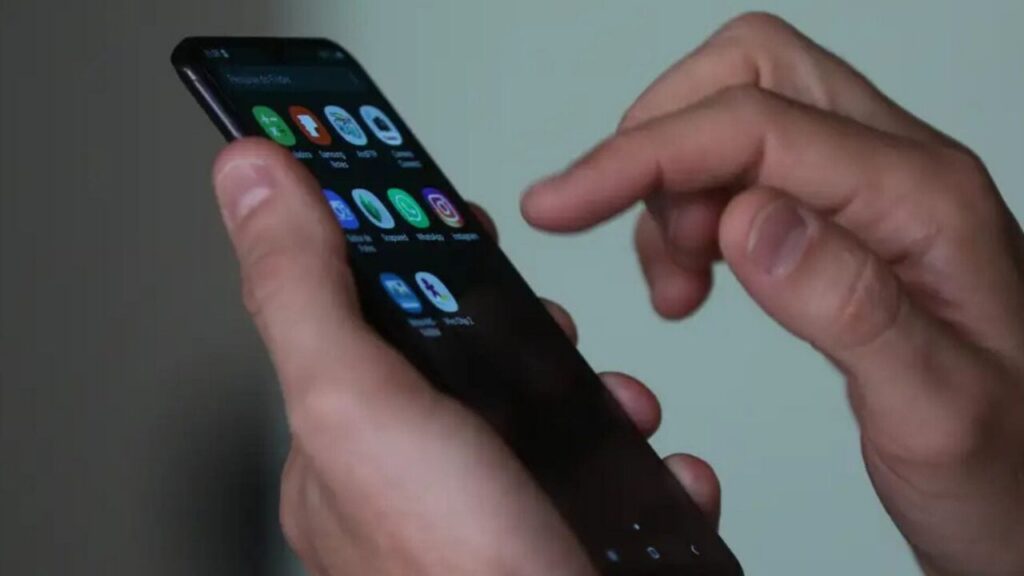 Um homem de terno segura um celular com aplicativos visíveis na tela