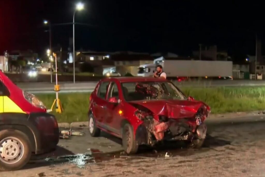 Um carro vermelho com a frente destruída após colisão em via noturna com outro veículo