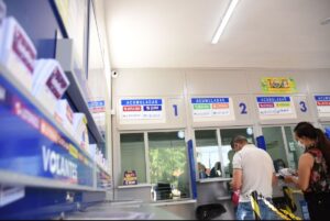Pessoas fazem apostas em frente a caixas de loteria com placas de jogos acumulados