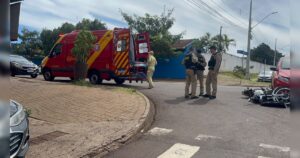 Um grupo de pessoas atende uma vítima em uma rua com uma ambulância e uma moto caída ao lado