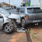 Carro prateado com frente destruída encostado em outro veículo após colisão em rua urbana