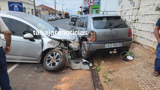 Carro prateado com frente destruída encostado em outro veículo após colisão em rua urbana