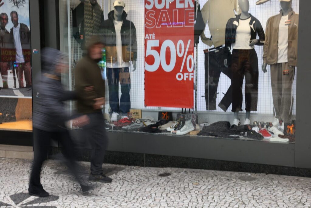 Um homem caminha em frente a uma vitrine de loja com promoção de até 50% de desconto
