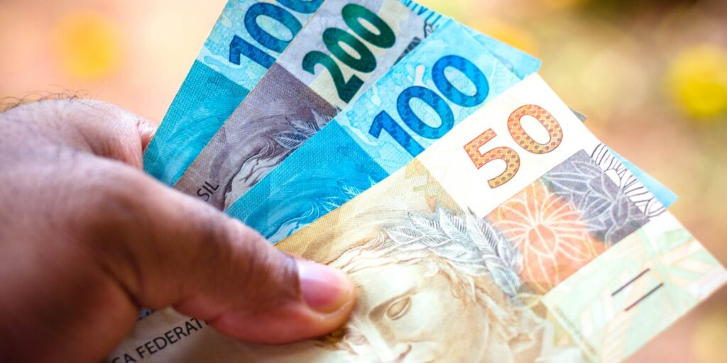Uma mão segura notas de real de diferentes valores em foco próximo