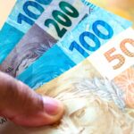 Uma mão segura notas de real de diferentes valores em foco próximo