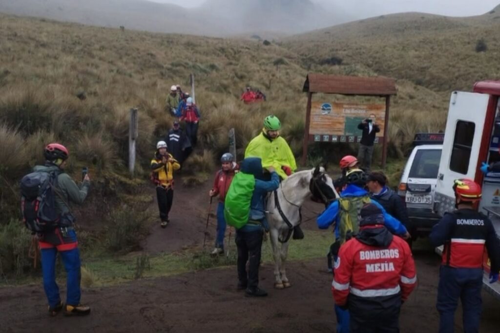 Um grupo de pessoas em uma trilha montanhosa com resgatadores e um cavalo próximo a uma ambulância